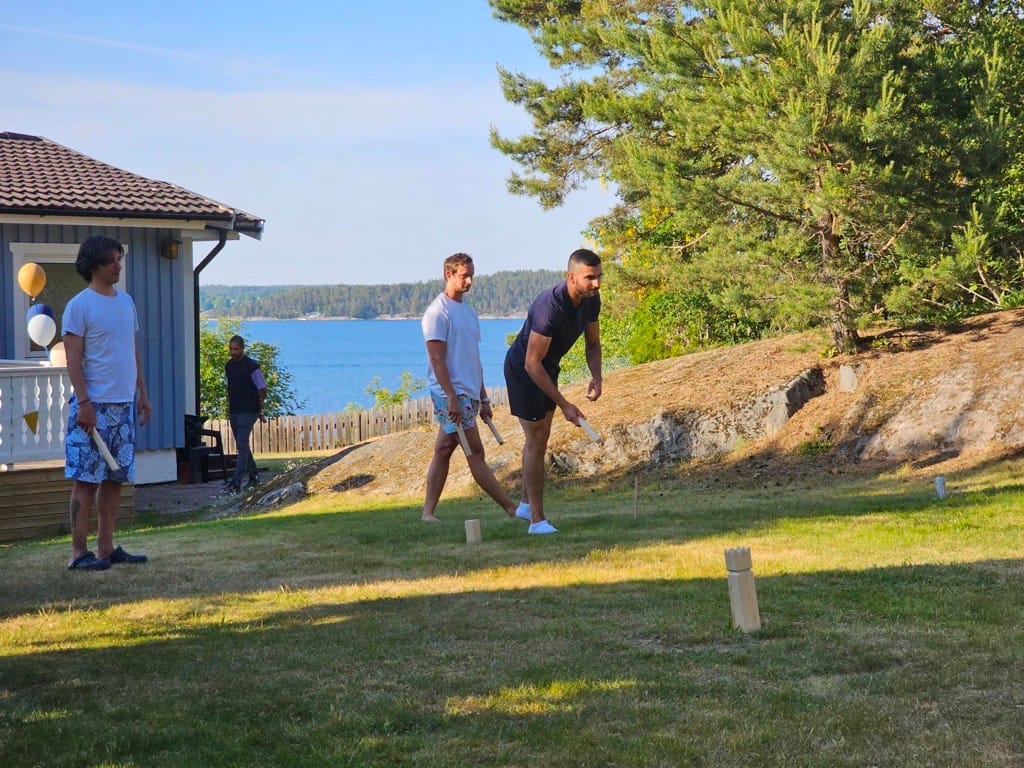 Colleagues playing kubb on a lawn by the water at the SwedQ summer party